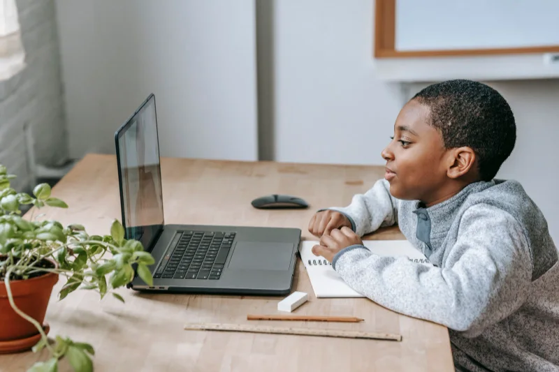 孩子在笔记本电脑前学习，桌面放着打开的笔记本
